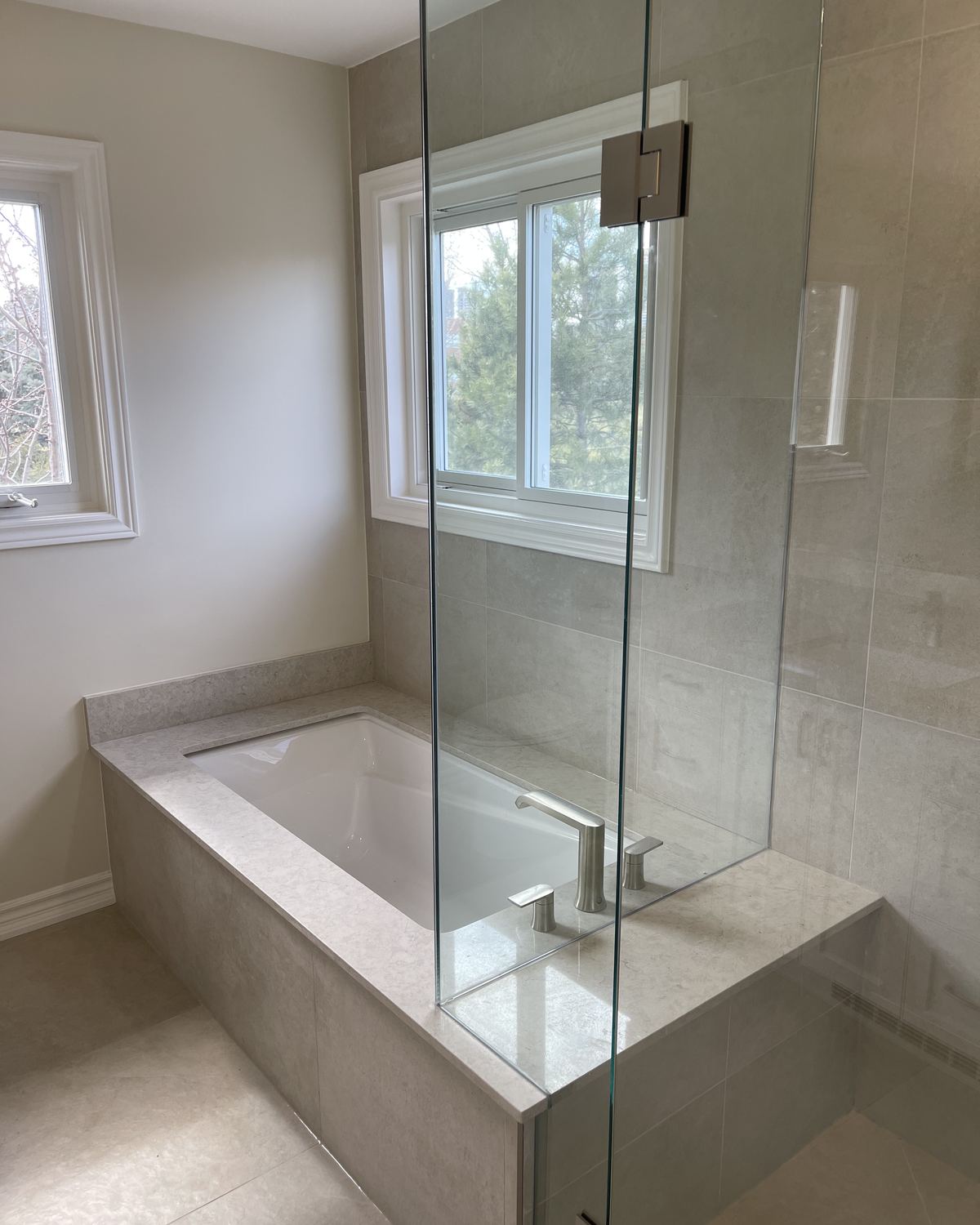 Renovated ensuite with a tiled soaker tub and frameless glass panel by Gdula Interiors